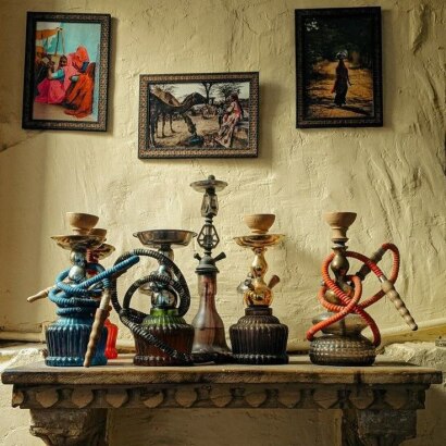 قلیان‌سرای سنتی با قلیان‌های آماده چوبی قدیمی روی میز چوبی و فضای گرم و تابلو و دکور شرقی